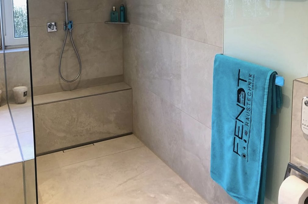 Helles, modernes Badezimmer mit einer großzügigen begehbaren Dusche. Die Wände und der Boden sind mit großen, beigen Fliesen gestaltet.
