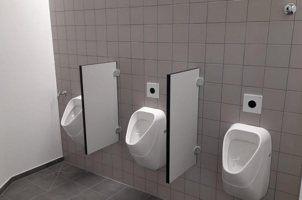 Sanitärbereich mit drei weißen Urinalen an einer grau gefliesten Wand